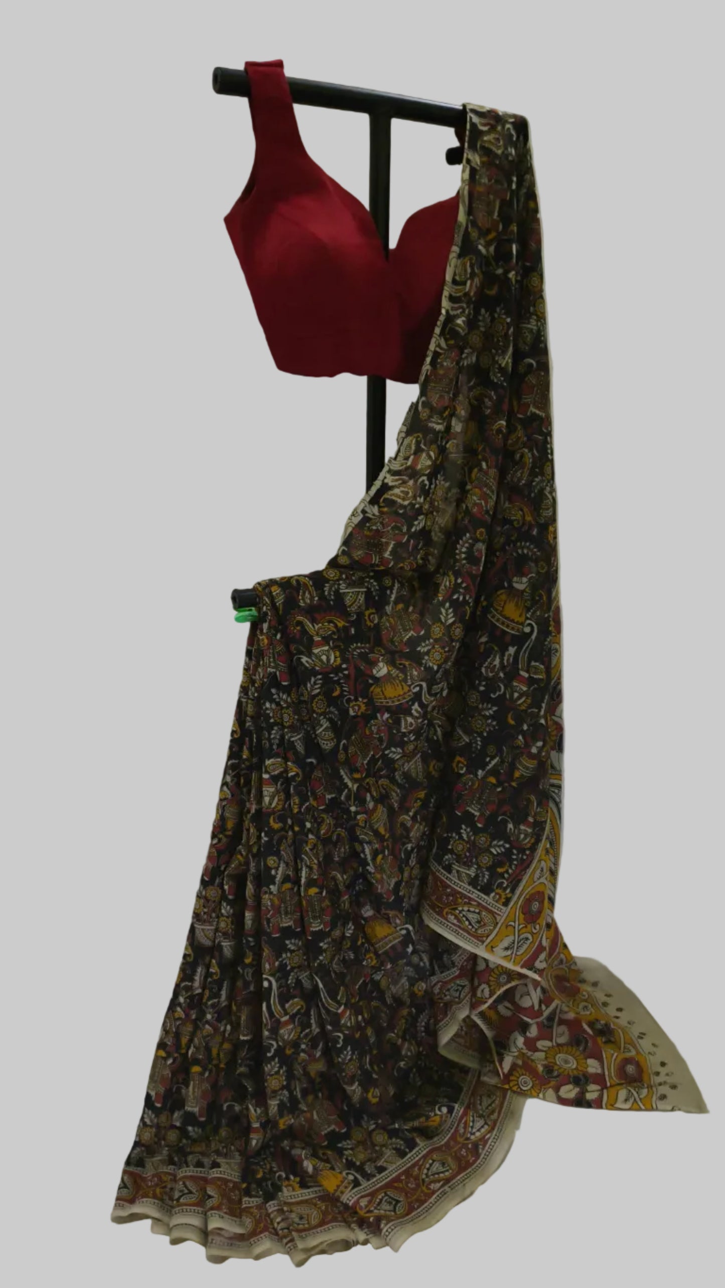 A traditional Indian saree with a dark brown and beige floral patterned body and border, draped on a black clothing stand, accompanied by a red sleeveless blouse.