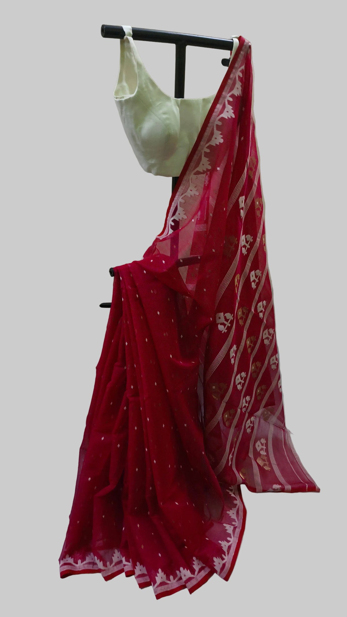 A red georgette saree with white floral patterns and a matching red blouse, displayed on a black clothing stand against a draped beige fabric backdrop.