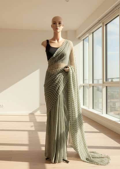 Mannequin wearing a green chiffon saree with a black top in a room with large windows.