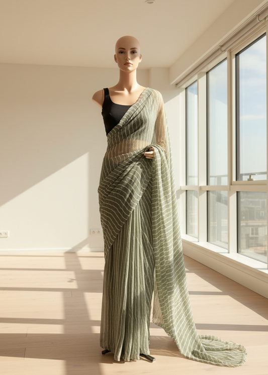 Mannequin wearing a green chiffon saree with a black top in a room with large windows.