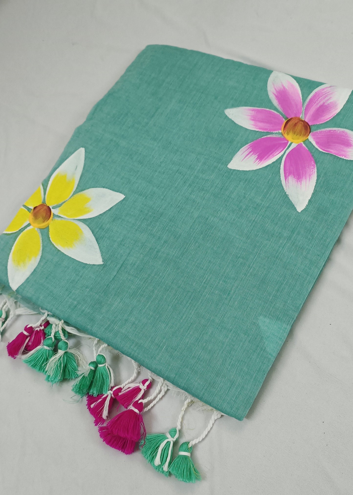 Turquoise fabric with floral designs and tassels on a light gray background