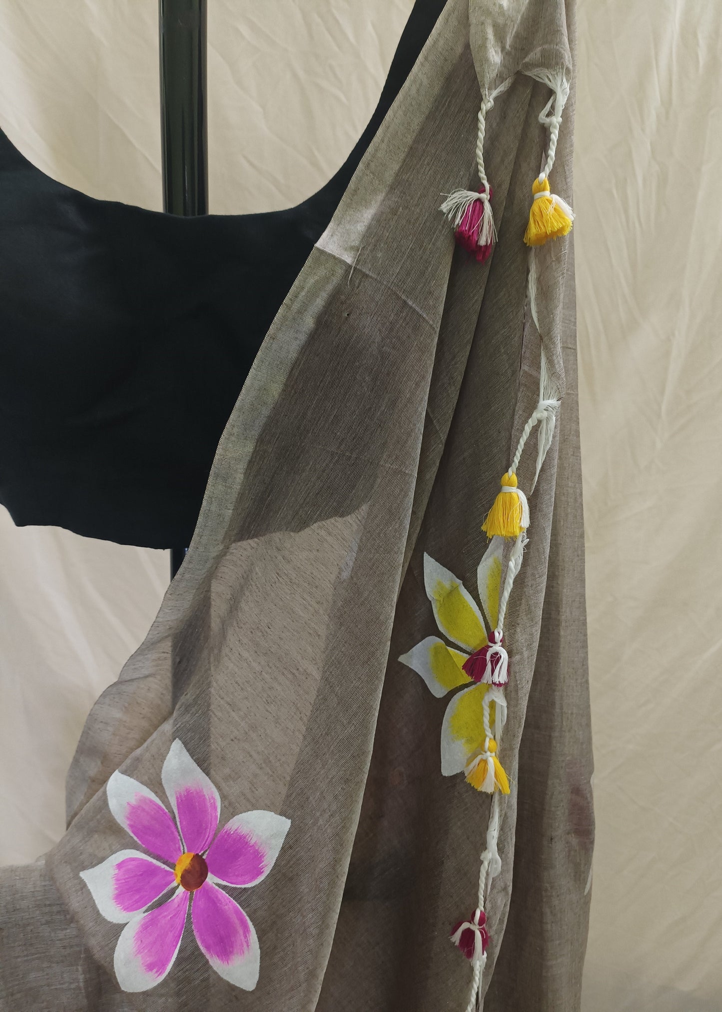 Brown saree with floral designs and tassels on a neutral background