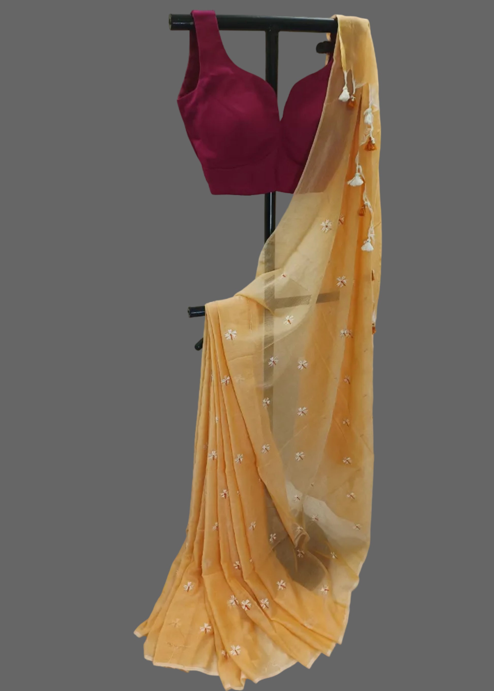 Yellow saree with a red blouse on a black stand against a white background