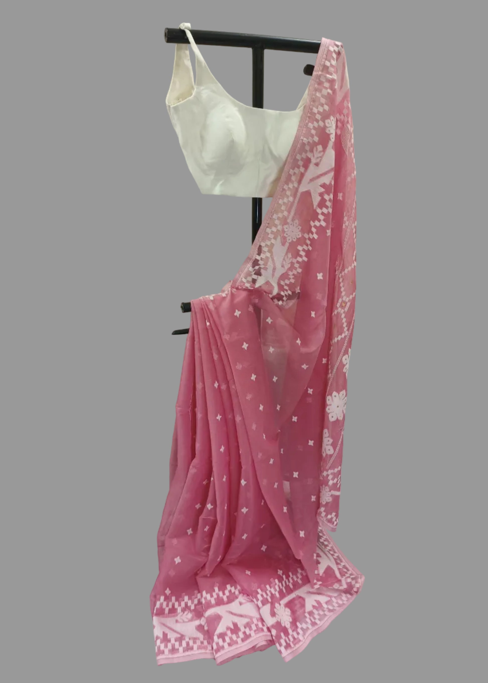Pink saree with white patterns draped over a black rod against a plain background