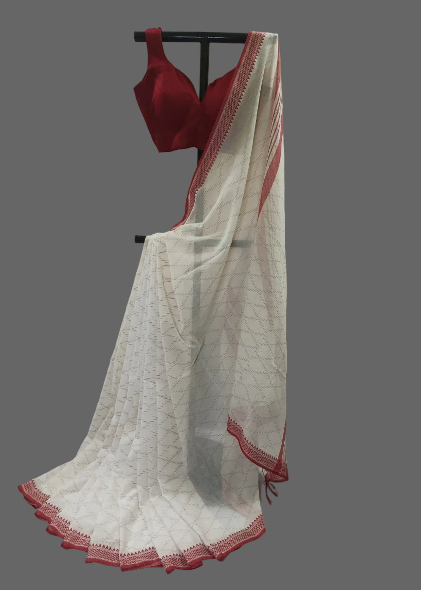 White saree with red border and red blouse on a mannequin against a plain background