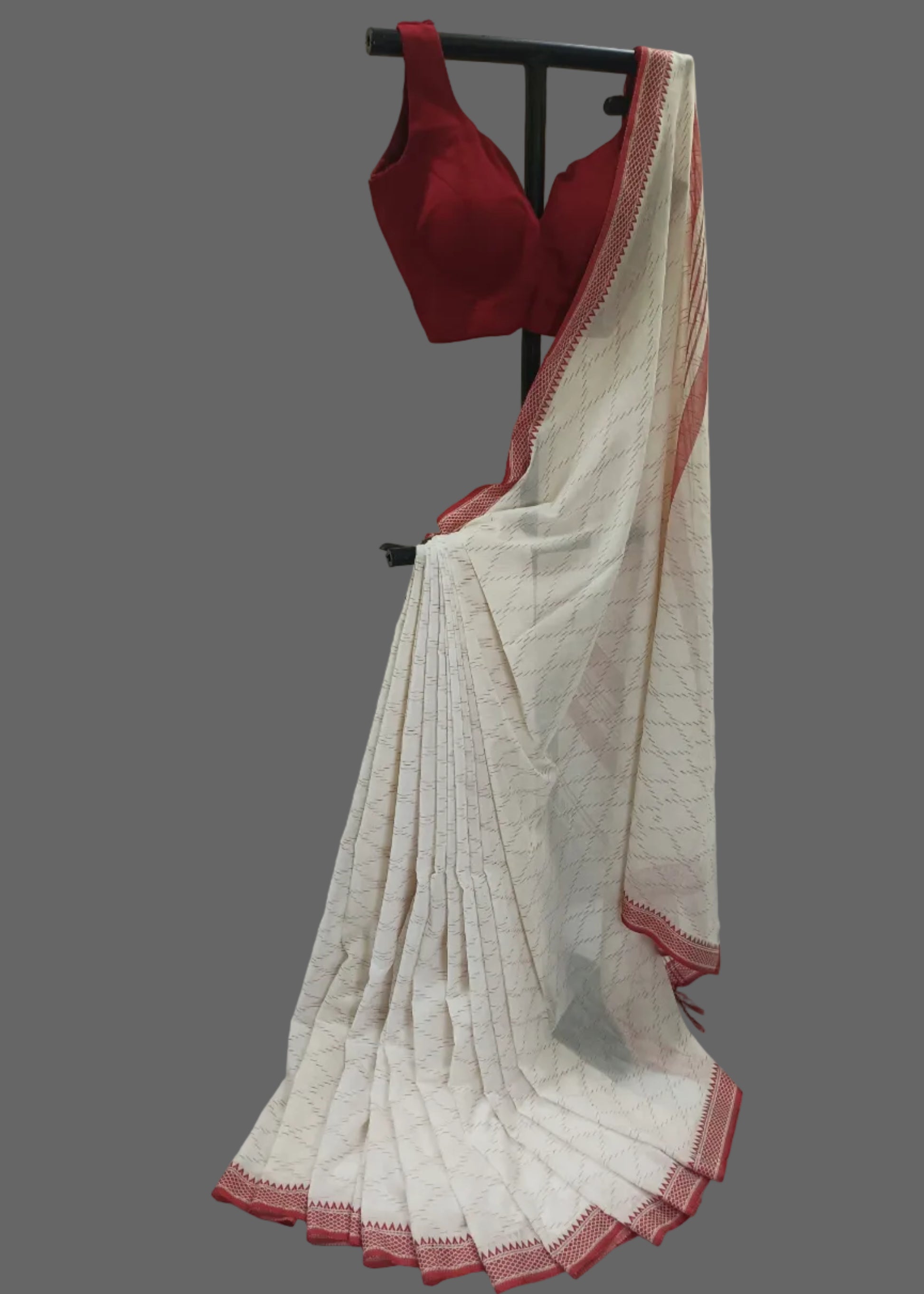 White saree with red border and red blouse on a stand against a white curtain background