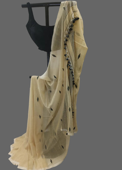 A cream-colored sheer saree with black leaf and border prints, draped over a black dress form against a white curtain backdrop.