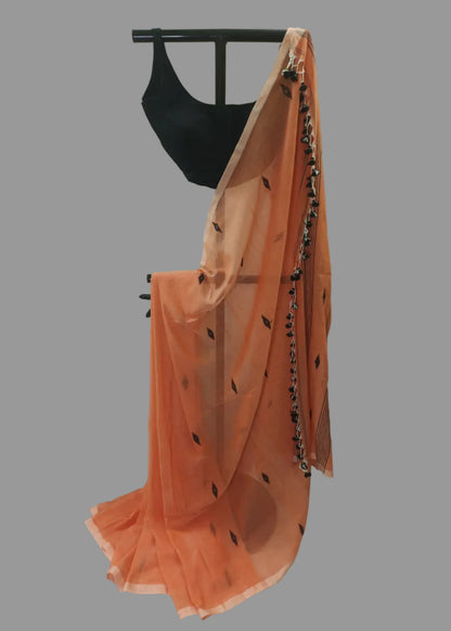 An orange georgette saree with black leaf prints and a black beaded border, draped on a black dress form with a black blouse against a white curtain backdrop.