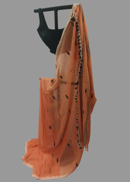 An orange saree with black leaf and border patterns draped over a black dress form, set against a white fabric backdrop.