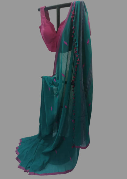 A teal green saree with pink border and small motifs, paired with a bright pink blouse, displayed on a black stand against a white fabric backdrop.
