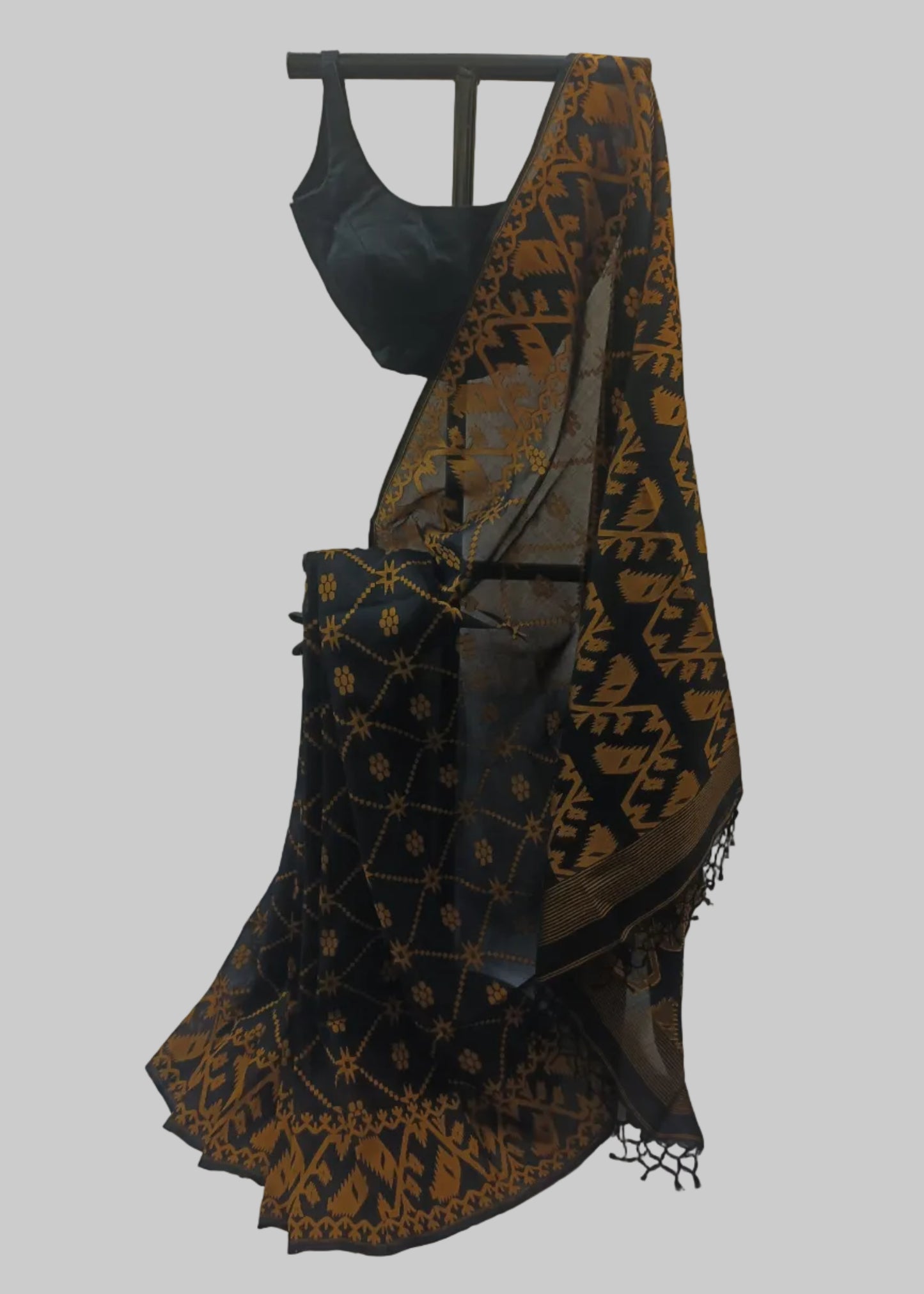 Black cotton saree with a gold ikat border and geometric pattern, paired with a black blouse, displayed on a hanger against a beige curtain backdrop.