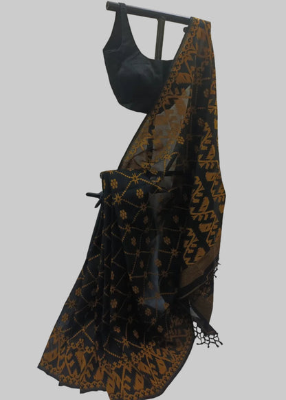 A black saree with a gold geometric and floral pattern, draped on a black hanger stand with a matching black blouse, set against a beige curtain backdrop.
