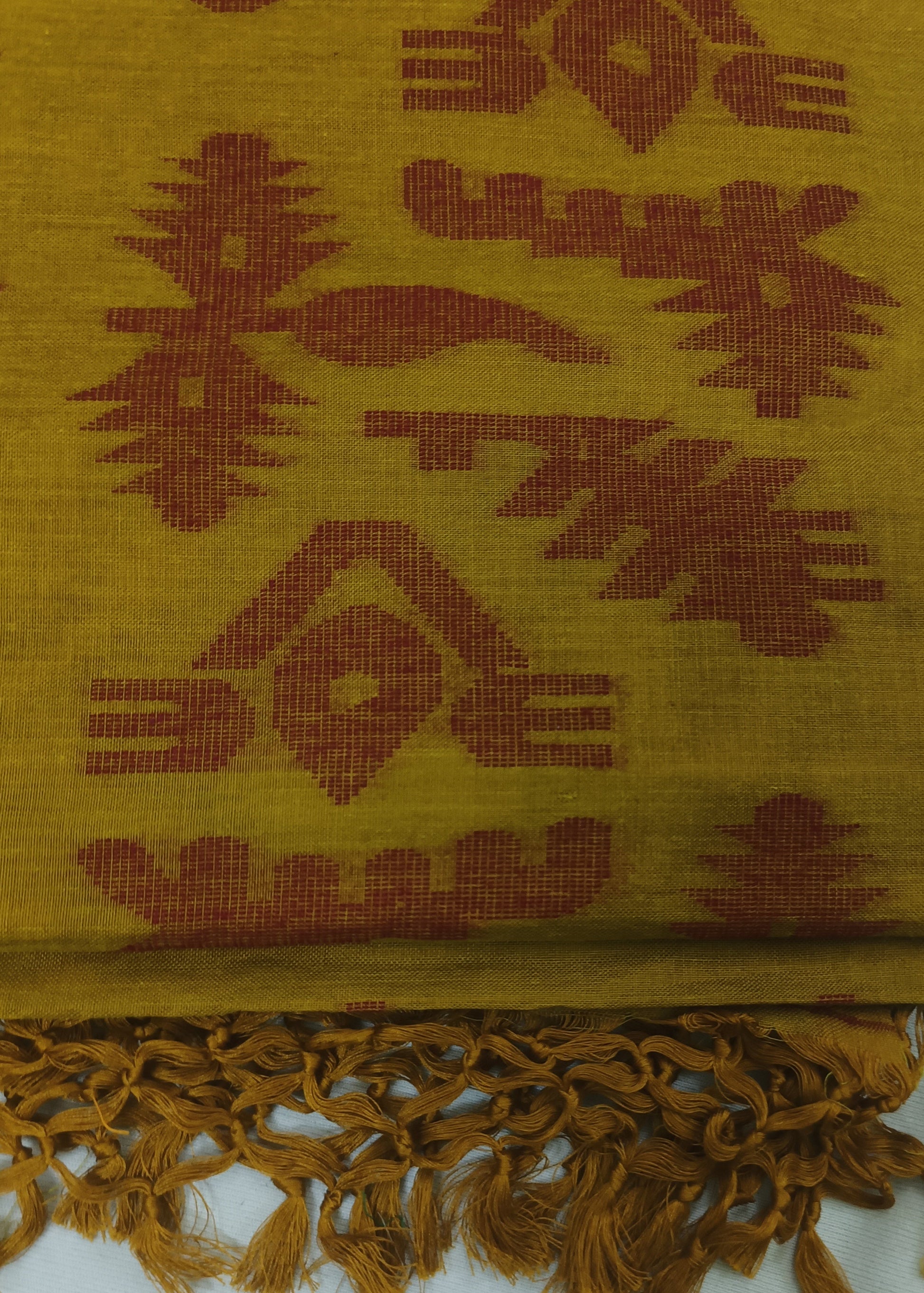A folded mustard yellow woven textile with a rust-brown geometric pattern and fringed tassels along one edge, shown on a white background.