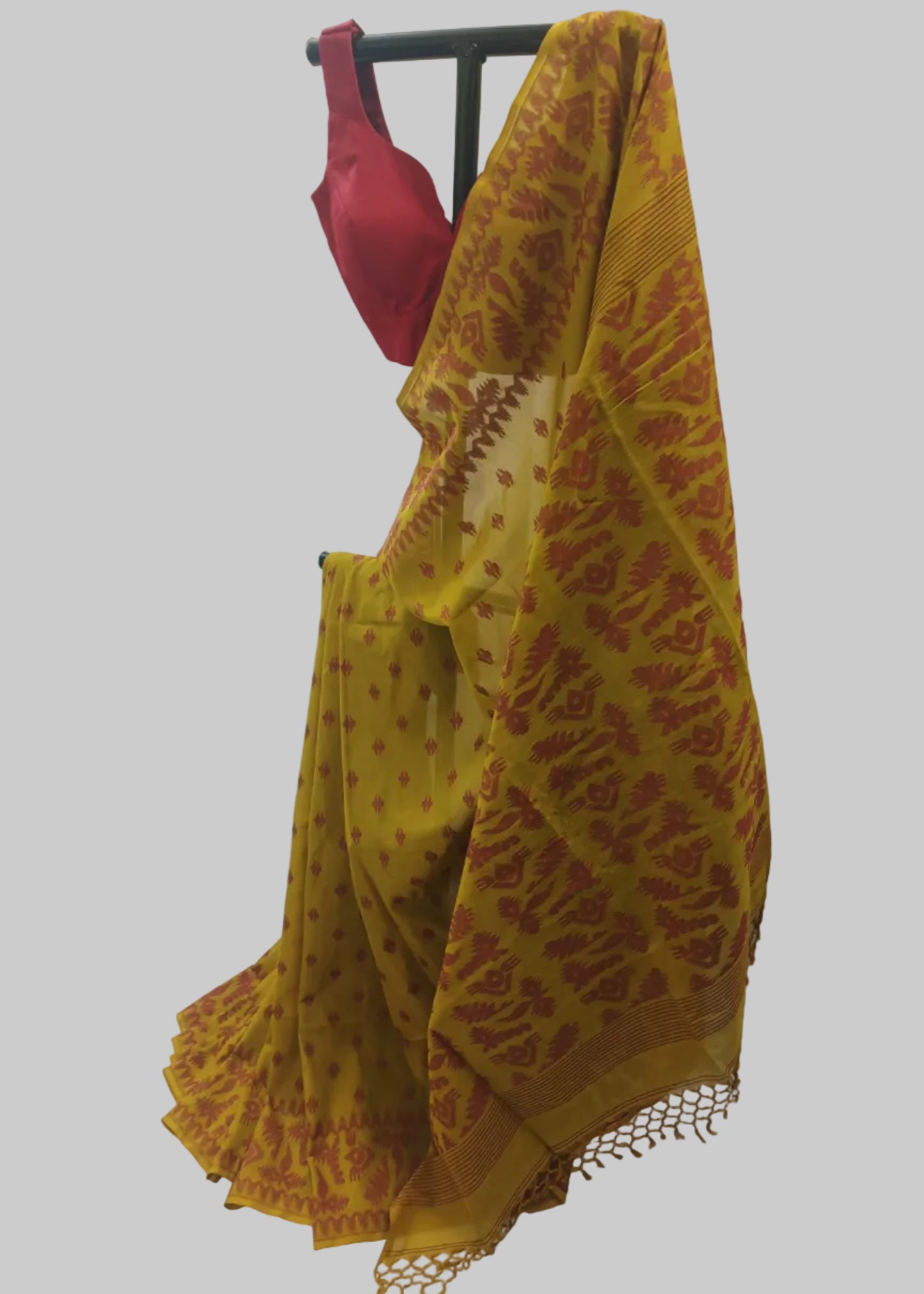 A yellow saree with a red floral pattern and a red blouse displayed on a black hanger against a white fabric backdrop.