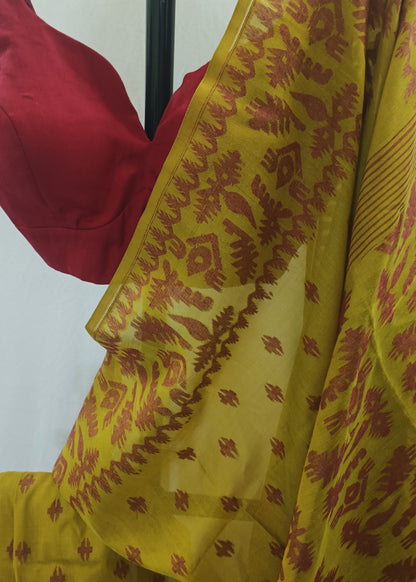 A yellow saree with a rust-red ikat pattern and border, draped over a black hanger with a red blouse visible at the top left, set against a plain off-white background.