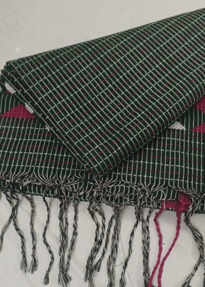 A folded dark green woven textile with white grid lines and fringed tassels, laid on a white fabric background. Pink patterned fabric is visible underneath at the edges.