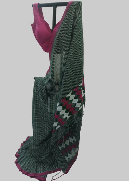 A dark green saree with a white grid pattern and a magenta-pink border, draped on a black hanger with a matching pink blouse visible at the top, set against a draped cream fabric backdrop.