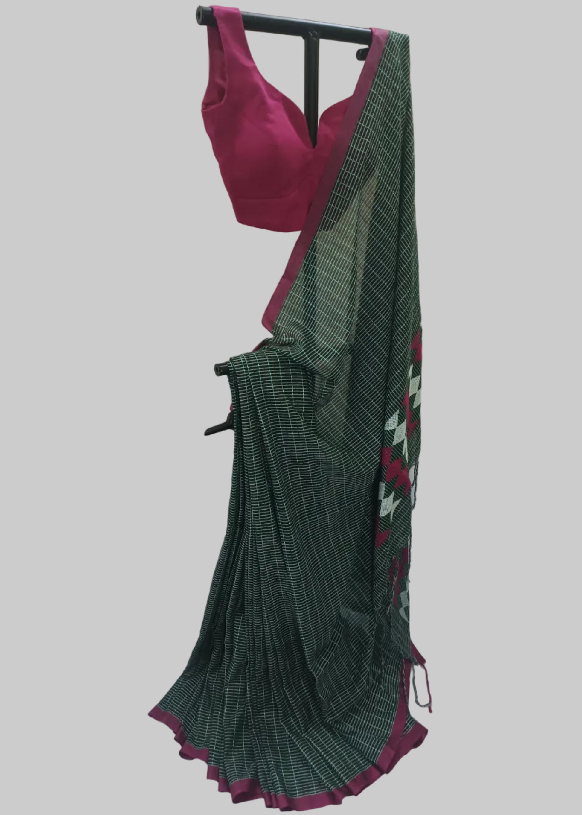 A dark green and black checkered saree with a magenta pink border and matching blouse, displayed on a black clothing hanger against a white draped backdrop.
