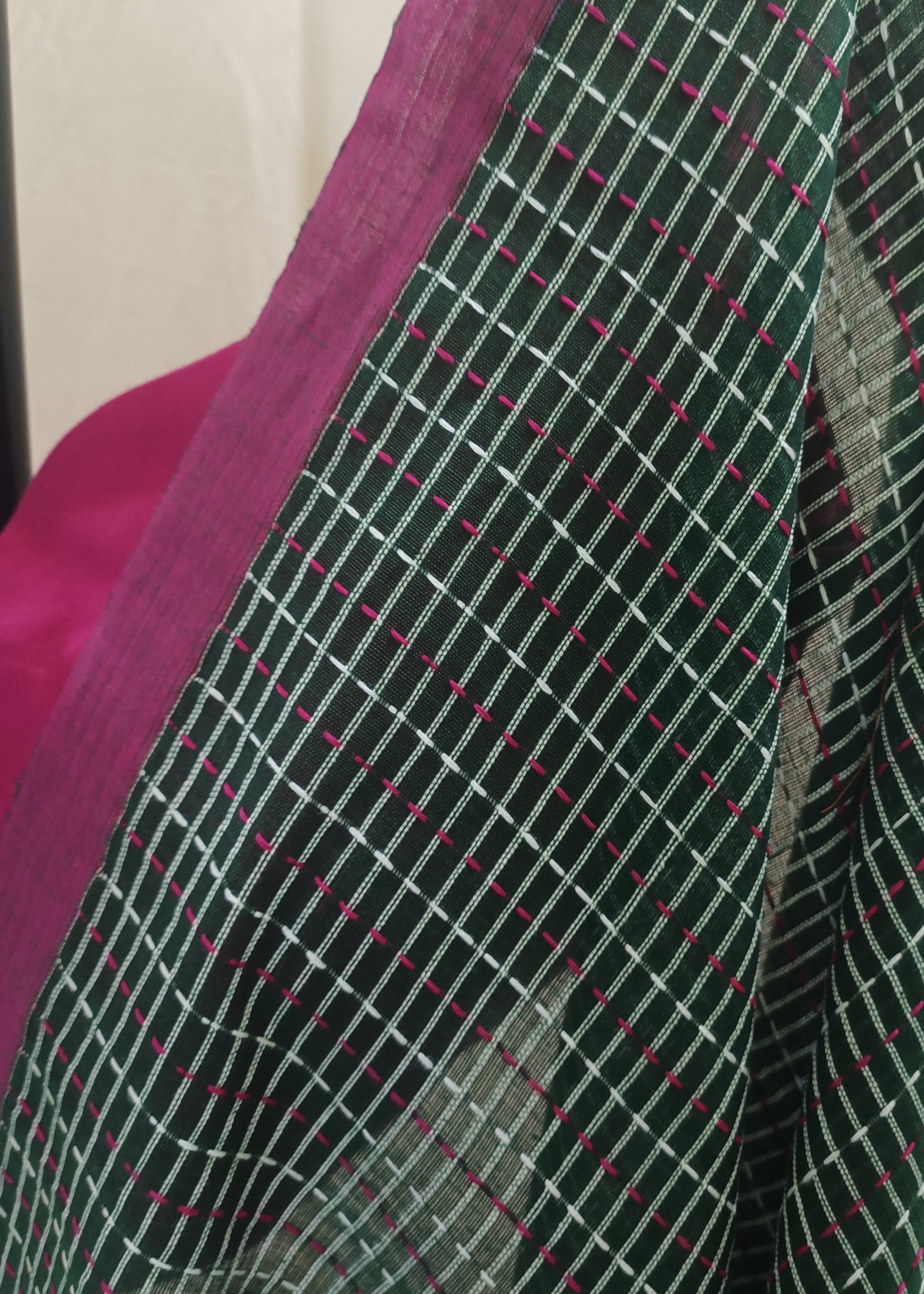 A close-up of a dark green saree fabric with a white grid pattern and small pink dotted lines, draped over a bright pink blouse.