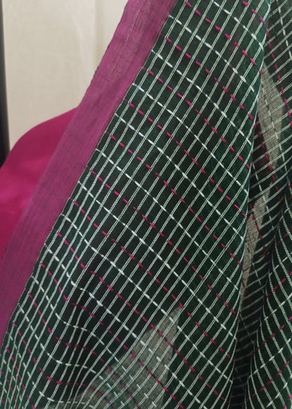 A close-up of a dark green saree fabric with a white grid pattern and small pink dotted lines, draped over a bright pink blouse.
