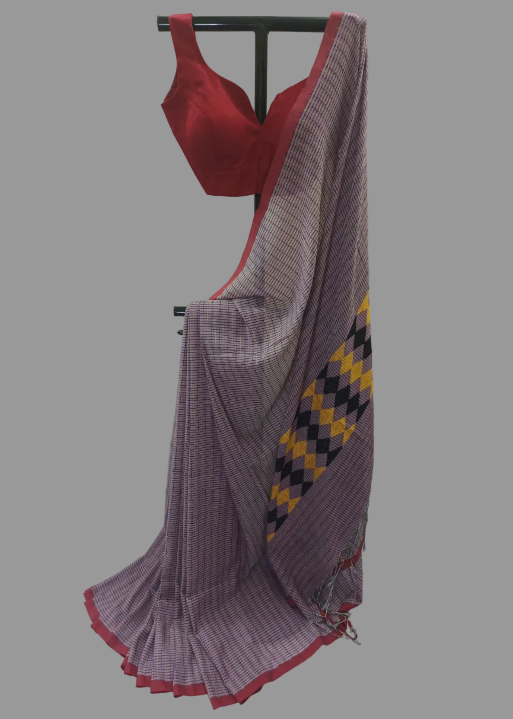 A purple and white checkered saree with a red border and a matching red blouse displayed on a black hanger against a white curtain backdrop.
