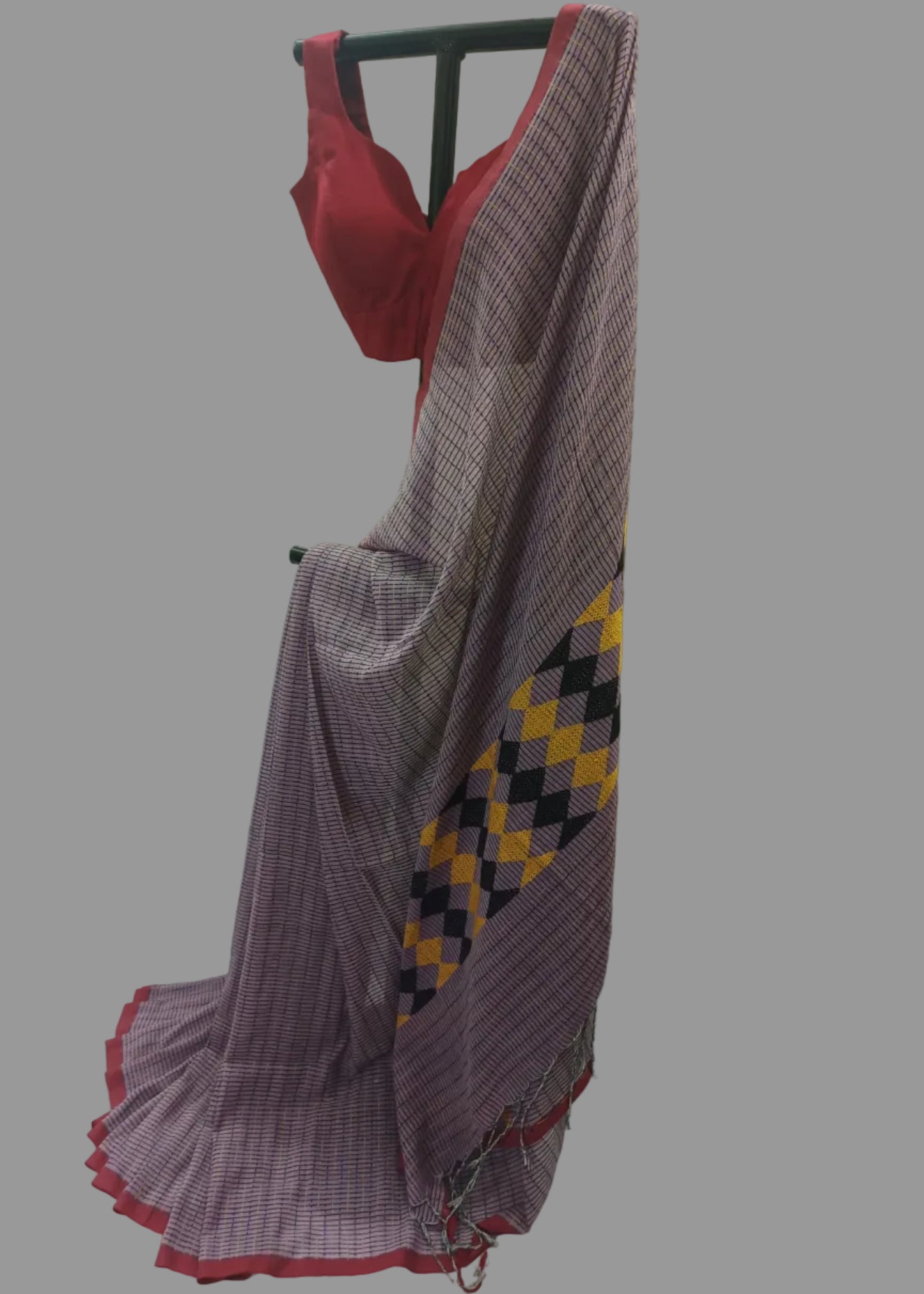 A purple and white checkered saree draped on a black hanger, paired with a red sleeveless blouse, set against a white draped backdrop.
