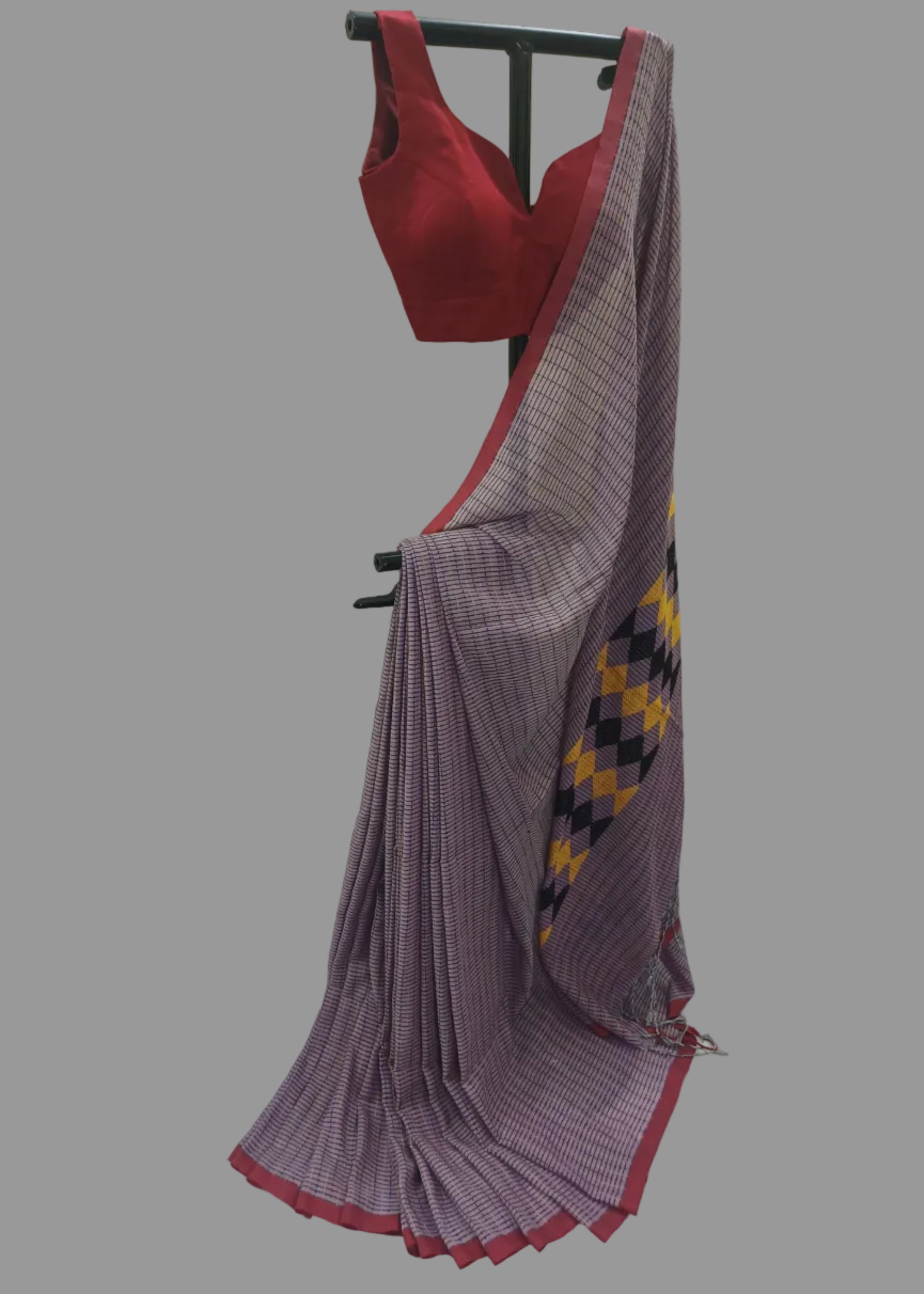 A purple and white checkered saree draped on a black clothing stand, paired with a red sleeveless blouse, set against a white draped fabric backdrop.