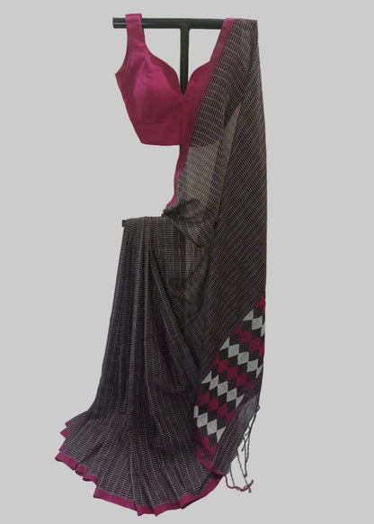 A dark gray and black checkered saree with a magenta pink border and matching blouse, displayed on a black hanger against a cream-colored curtain backdrop.