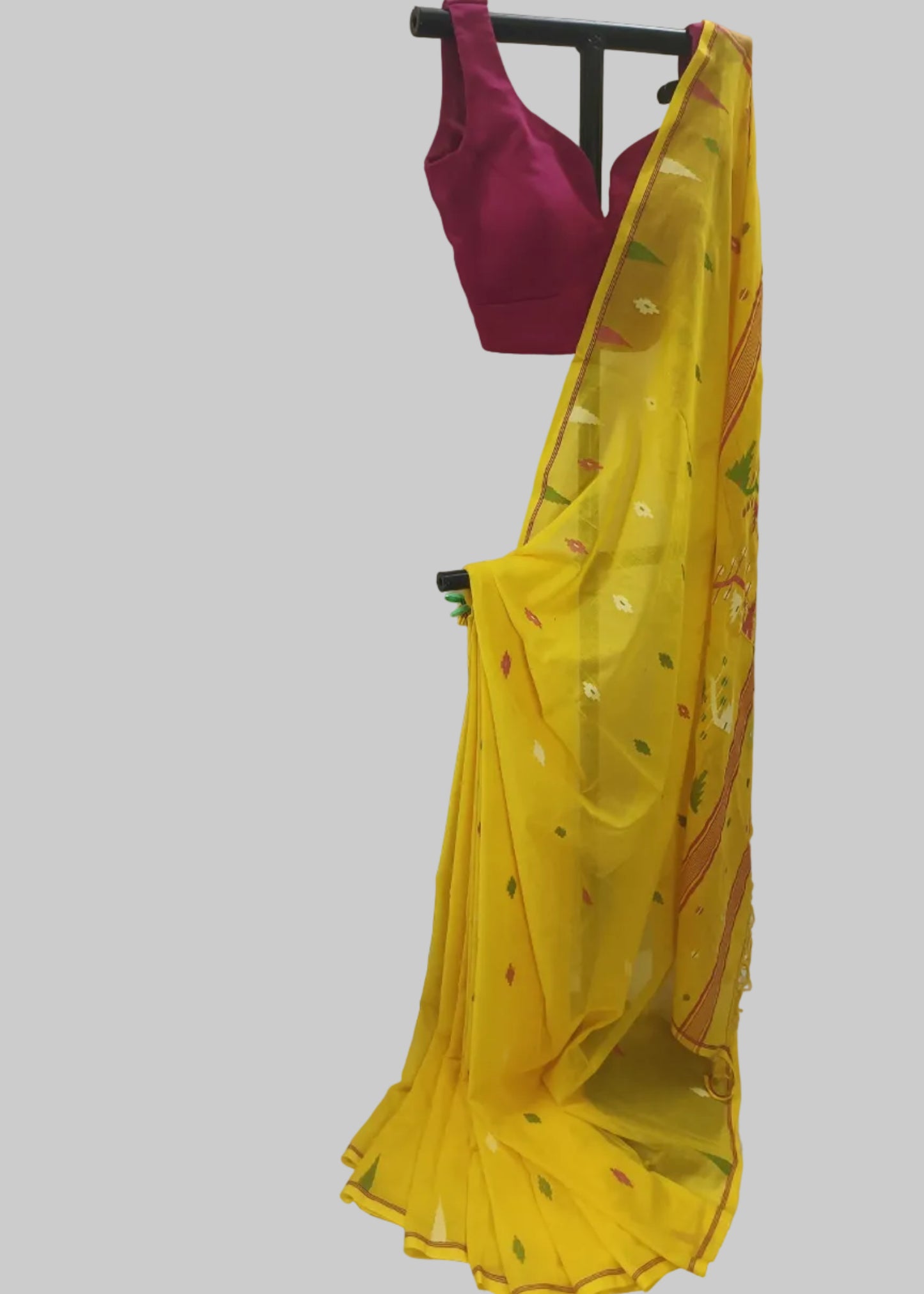 A yellow saree with small multicolor floral prints and a matching magenta pink sleeveless blouse, displayed on a black hanger against a white fabric backdrop.