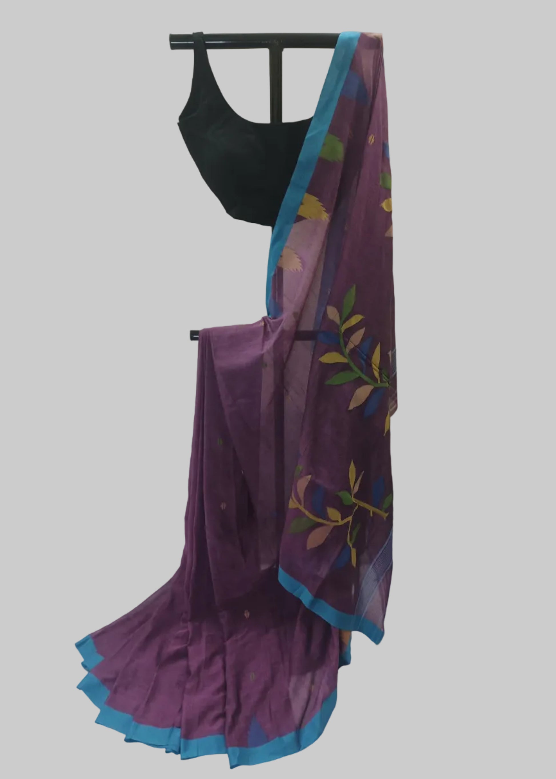 A purple saree with a blue border and multicolor floral print, paired with a black blouse, displayed on a stand against a white fabric backdrop.