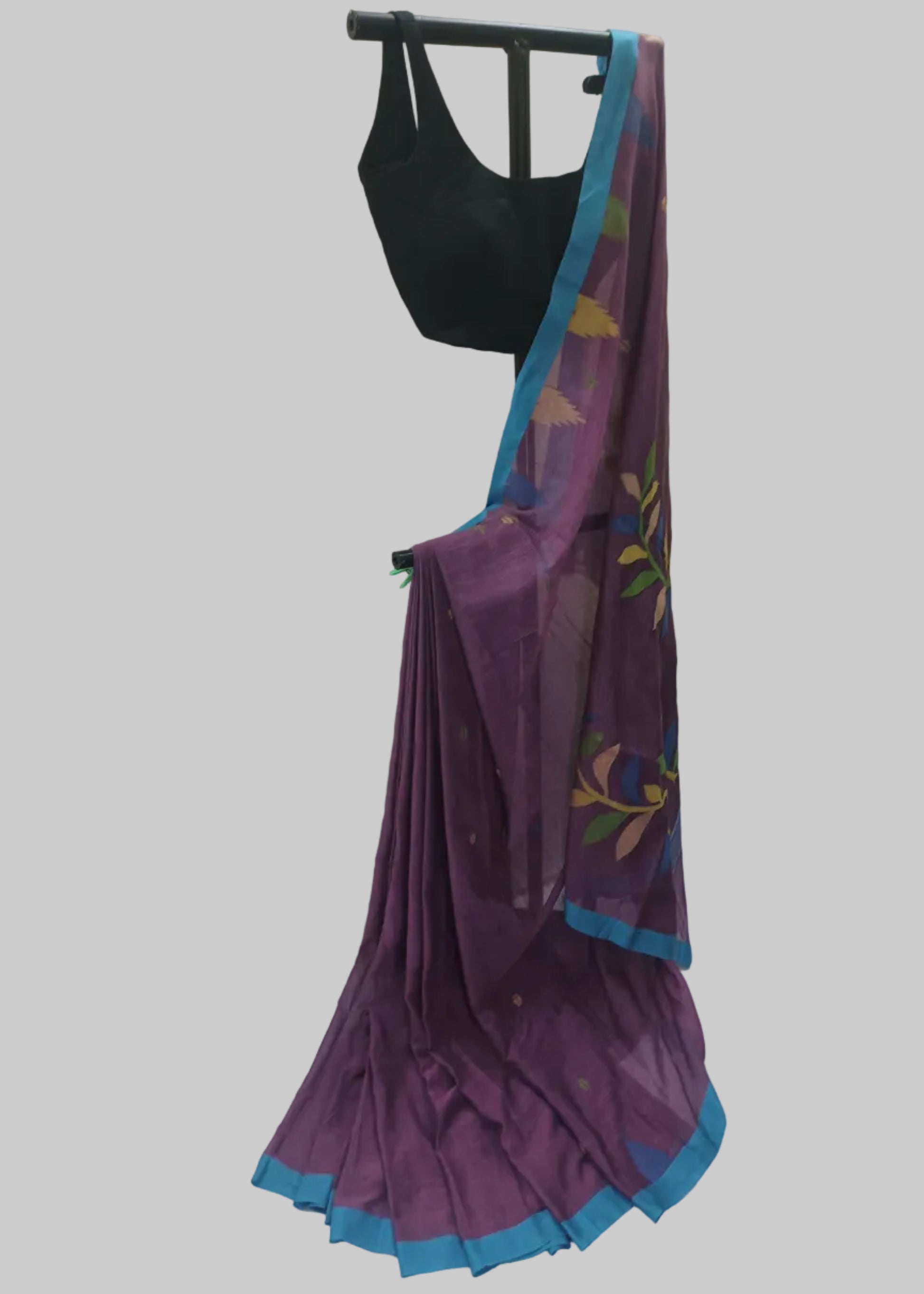 A purple silk saree with a blue border and colorful floral motifs, draped over a black blouse hanger against a white fabric backdrop.
