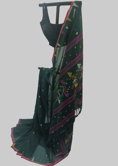 A dark green saree with pink border stripes, multicolor floral prints, and small dotted motifs, draped on a black dress form with a black blouse. The backdrop is a white fabric sheet.