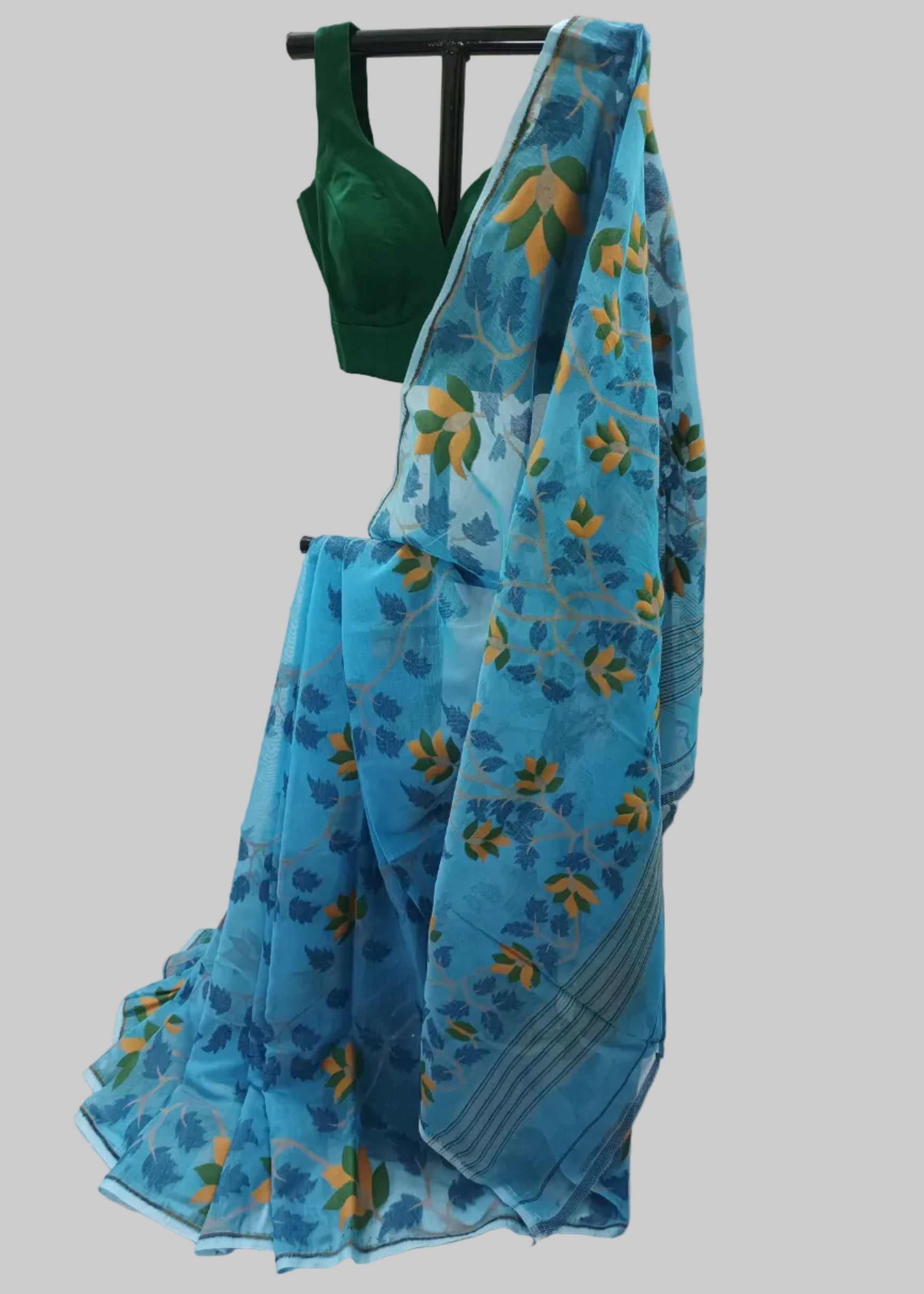 A blue patterned saree draped on a black hanger stand, paired with a dark green blouse, set against a white fabric backdrop.