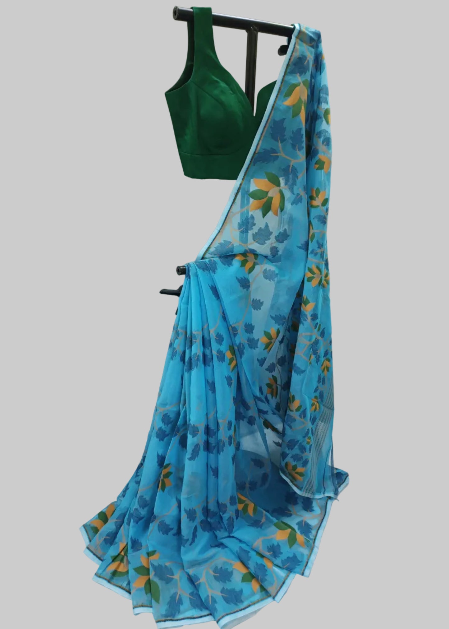A blue floral printed saree draped on a black clothing rack, paired with a dark green sleeveless blouse, set against a white fabric backdrop.