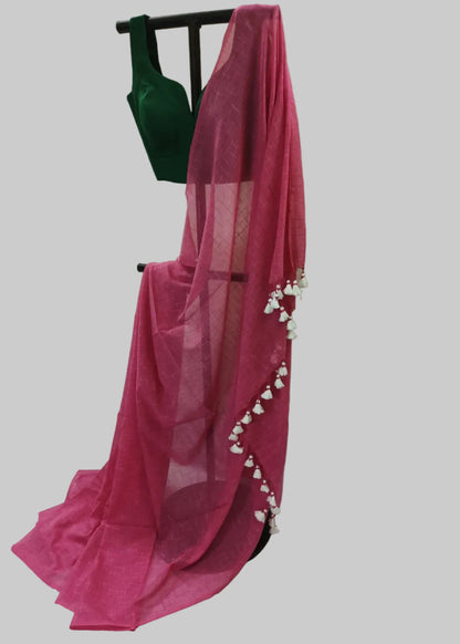 A pink sheer saree draped over a black hanger with a dark green sleeveless blouse, decorated with white floral tassels along the border, set against a solid gray background.