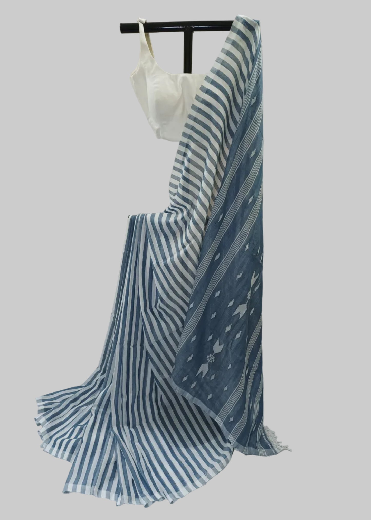 A blue and white striped saree draped on a black dress form with a white blouse, set against a draped white fabric backdrop.