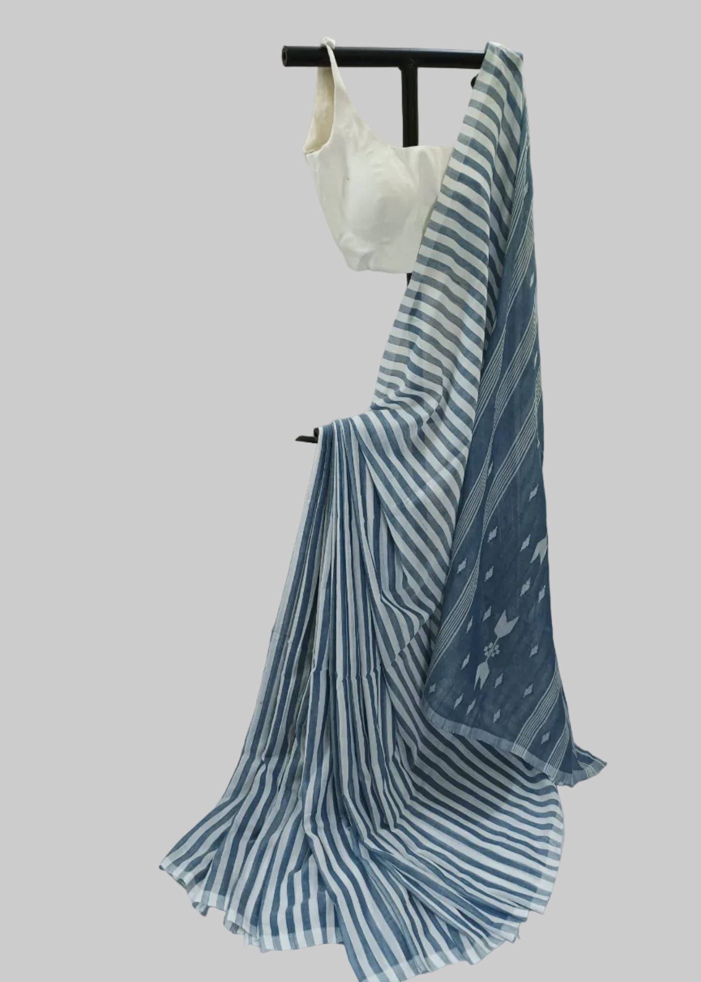 A blue and white striped saree draped over a black hanger with a white blouse, set against a draped white fabric backdrop.