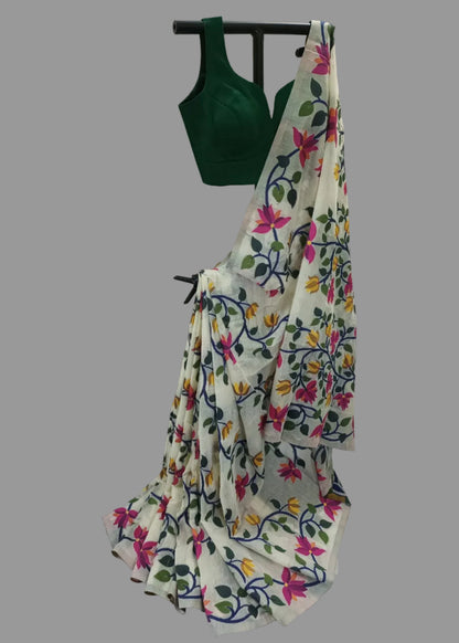 A white saree with a vibrant multicolor floral print, paired with a dark green sleeveless blouse, displayed on a black hanger against a white draped fabric backdrop.