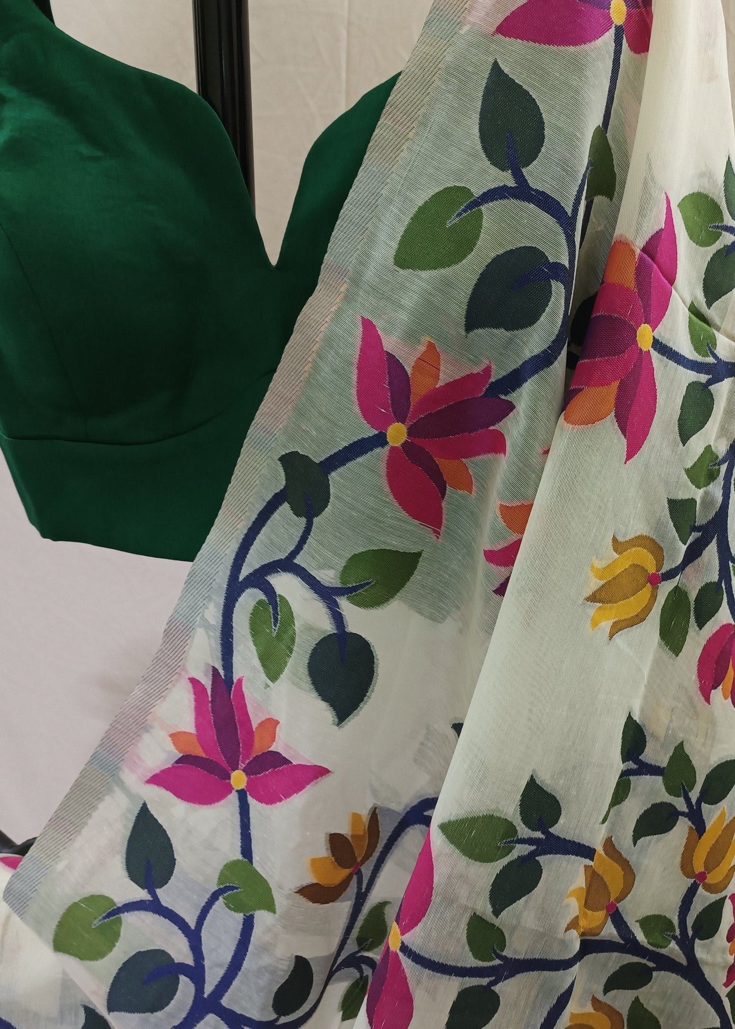A white organza saree with vibrant floral and vine patterns in pink, yellow, green, and blue, draped over a dark green blouse.