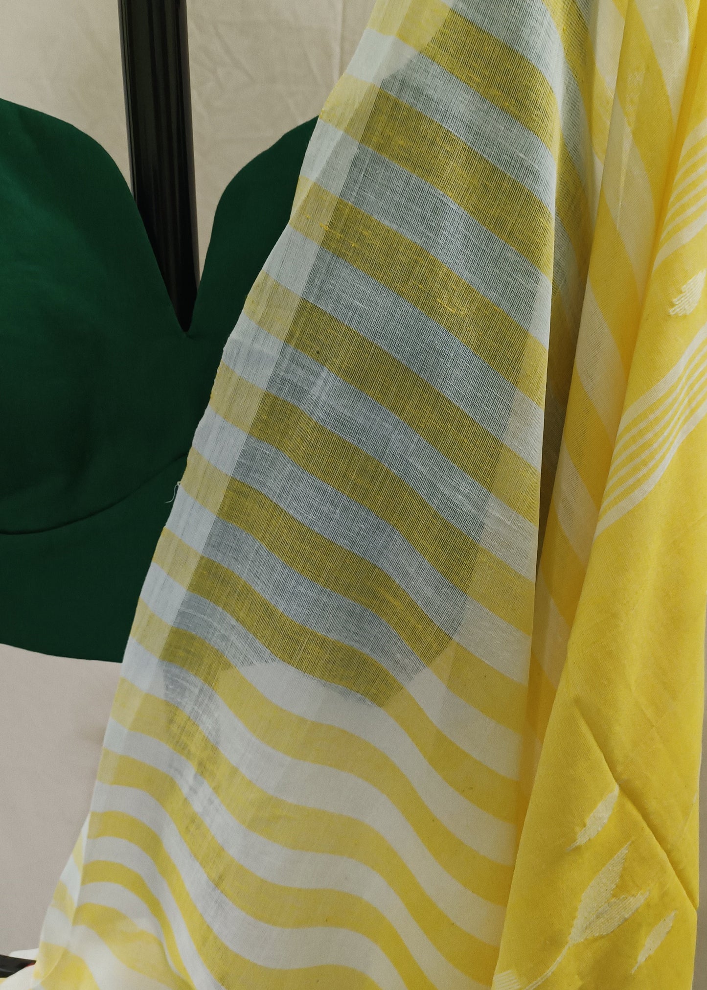 Yellow and white striped saree fabric draped over a dark green blouse, shown against a light beige fabric backdrop.