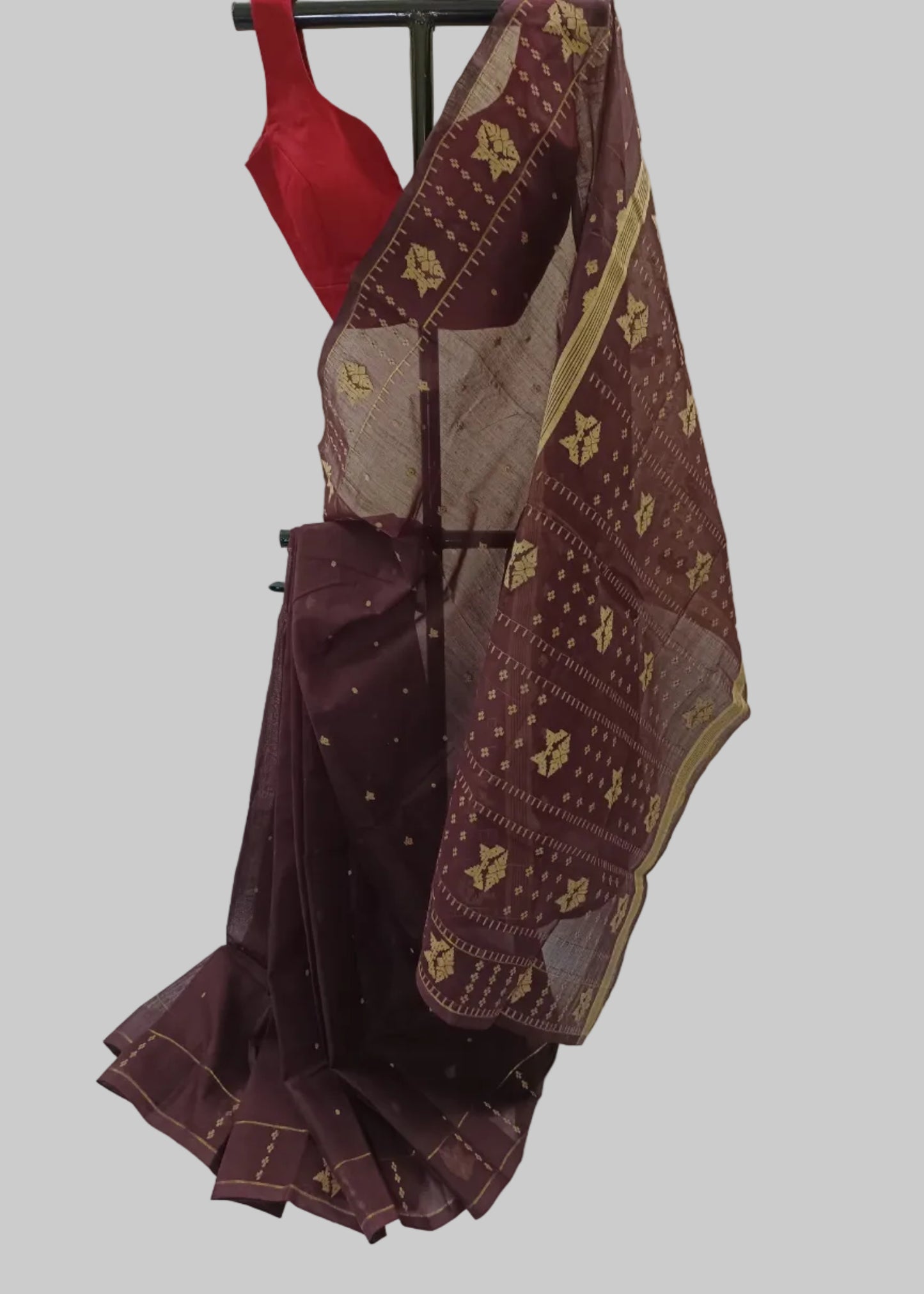A dark maroon silk saree with gold zari patterns and a red blouse, displayed on a black hanger against a white draped fabric background.