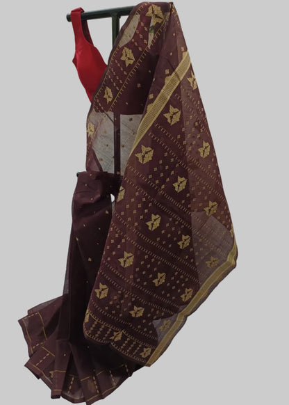 A dark maroon silk saree with gold geometric patterns and a red blouse, displayed on a black hanger against a draped white fabric backdrop.