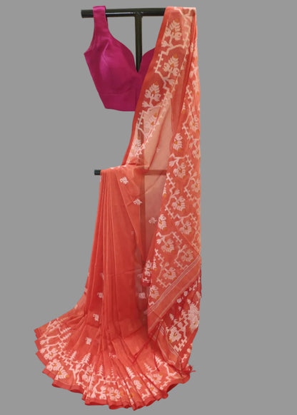 A coral orange georgette saree with white floral prints and a matching magenta pink blouse, displayed on a black clothing stand against a white fabric backdrop.