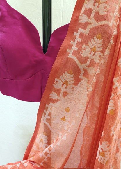 A close-up of a peach-orange saree with a white and yellow floral block print, draped over a magenta pink blouse on a black hanger against a white background.