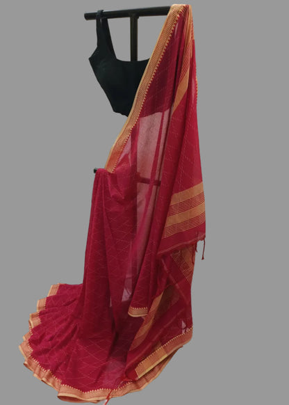A deep red saree with a gold border and a matching red blouse displayed on a black hanger against a draped white fabric backdrop.