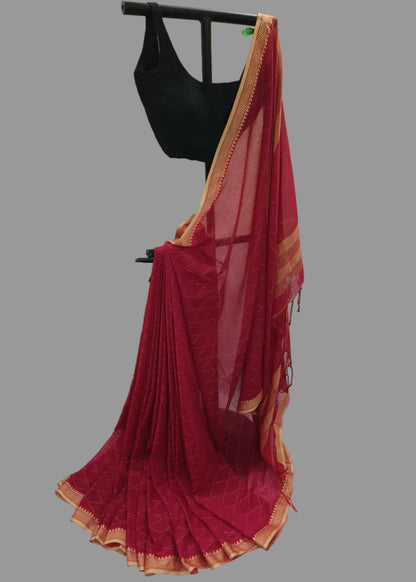 A deep red saree with gold zari borders draped on a black hanger stand, paired with a black sleeveless blouse, set against a white draped fabric backdrop.