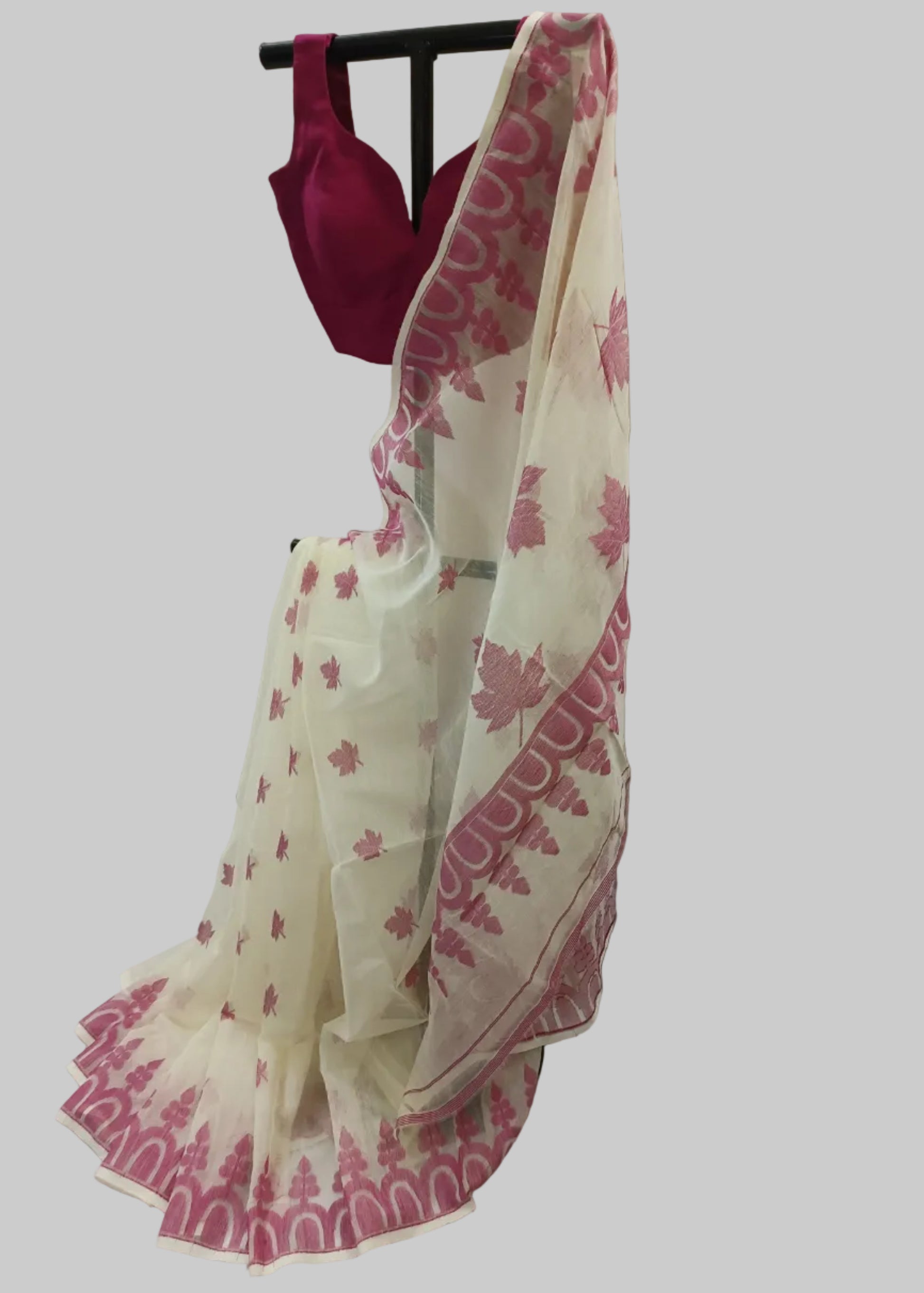 An off-white georgette saree with pink floral and border patterns, paired with a deep pink blouse, displayed on a black hanger against a draped beige fabric backdrop.