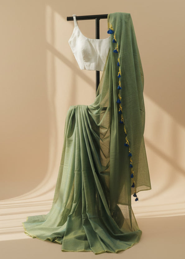 Green saree with a white blouse on a mannequin against a beige wall.