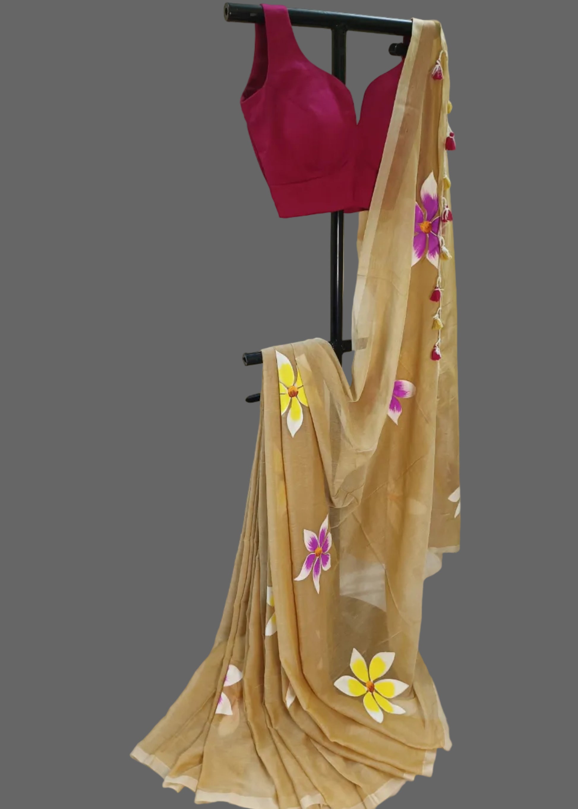 Beige saree with floral patterns draped over a pink blouse on a stand against a plain background.