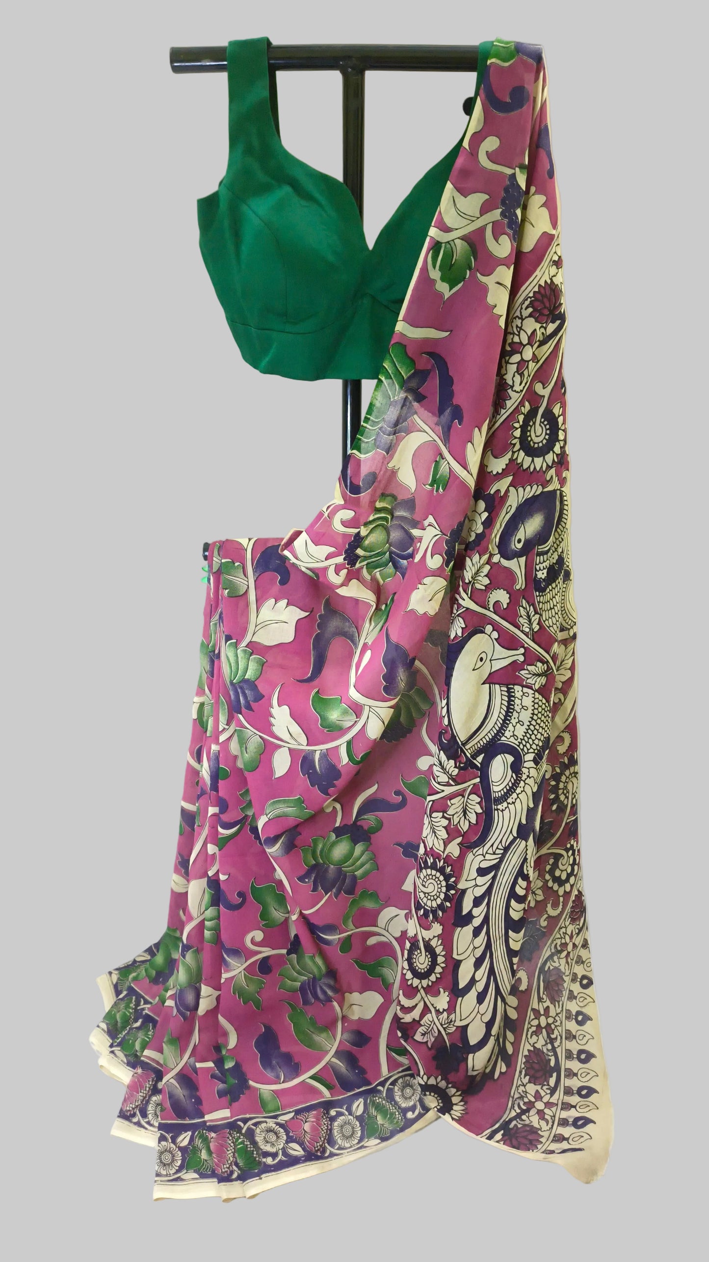 A pink and green printed saree draped on a black dress form, paired with a solid green blouse, set against a white draped fabric background.